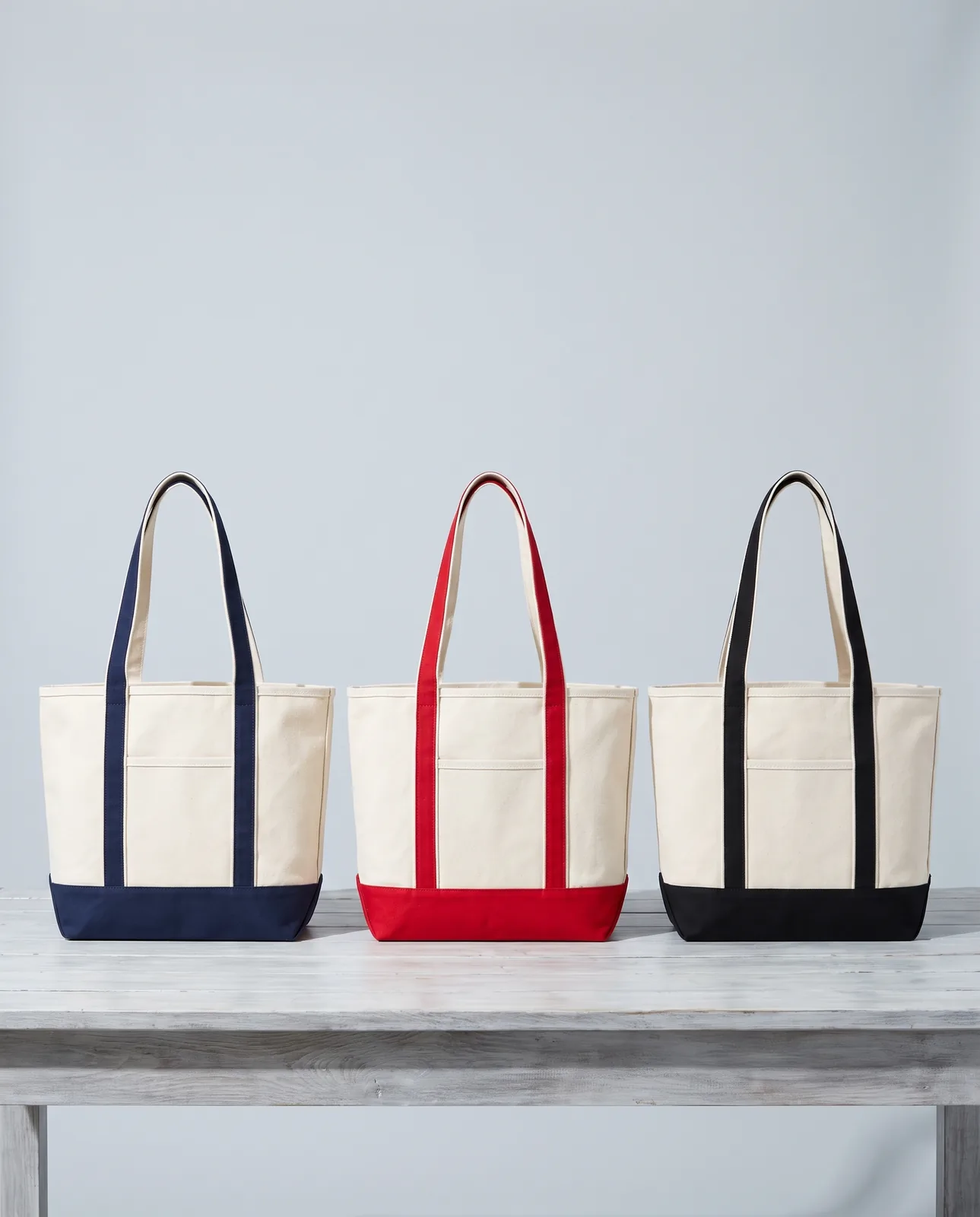 Custom canvas tote bags in Natural / Navy Blue, Red and Black lined up on a driftwood table