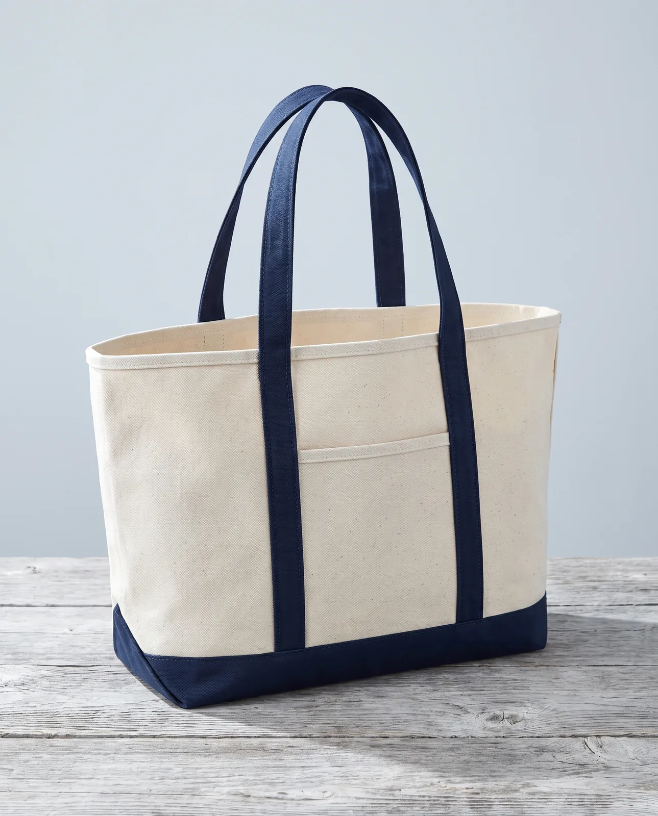 Custom canvas tote bags in Natural / Navy Blue, 18 oz cotton boat tote standing on a driftwood table