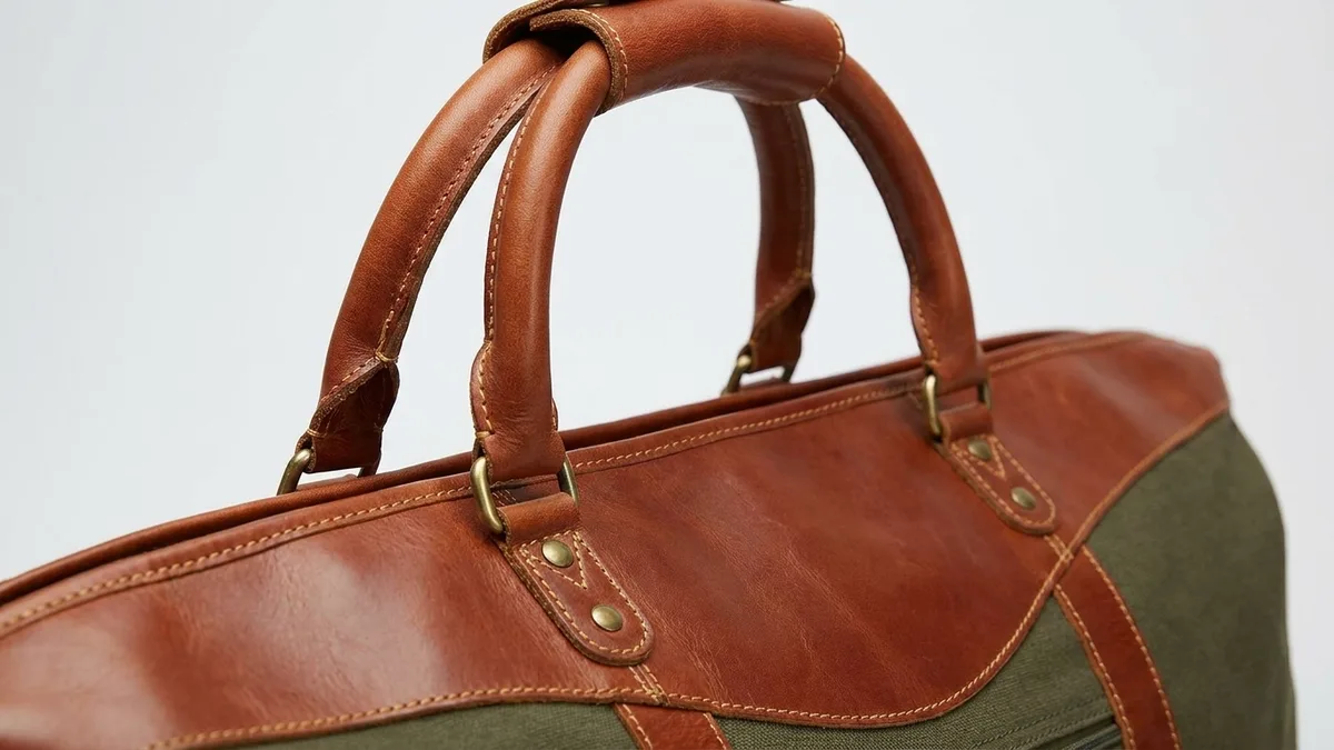 Rolled cognac leather carry handles with antique brass hardware on a custom leather duffel bag — Brandevois