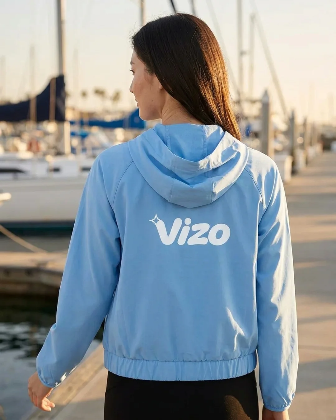 Back of a custom hooded sun shirt in Columbia Blue at a marina, with a logo printed across the upper back below the hood