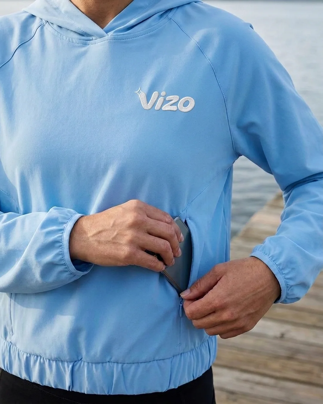 Close-up of a custom sun shirt in Columbia Blue with a phone going into the zip pocket, elastic cuffs and hem, and a stitched chest logo