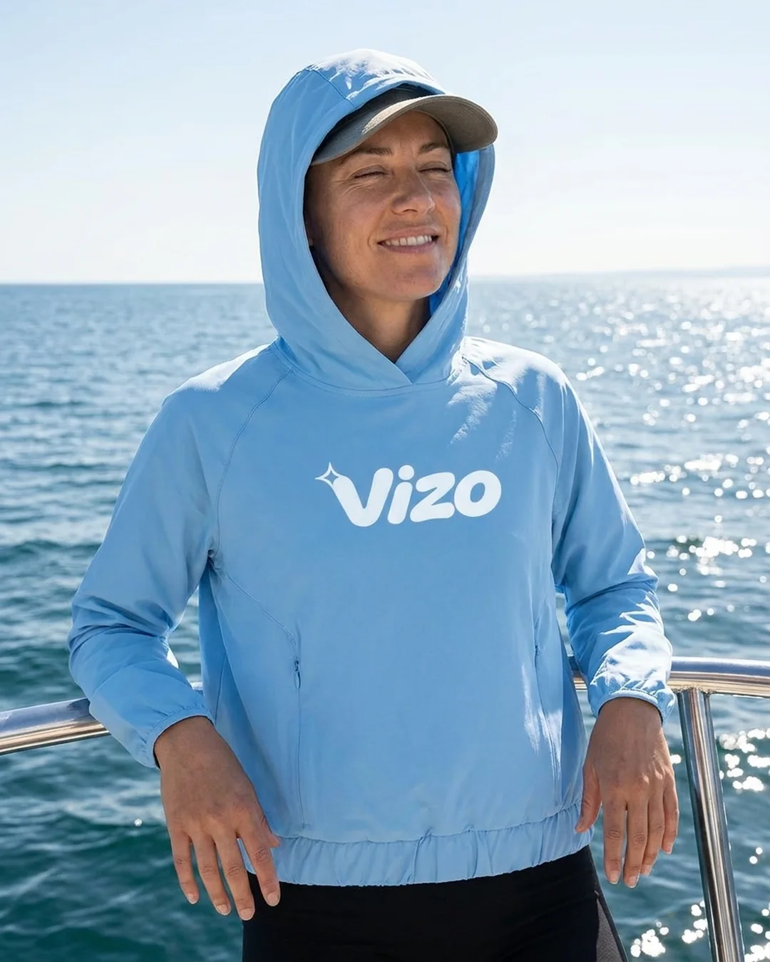 Woman on a charter boat wearing a custom sun shirt in Columbia Blue with the hood up over a cap and a white logo printed across the front
