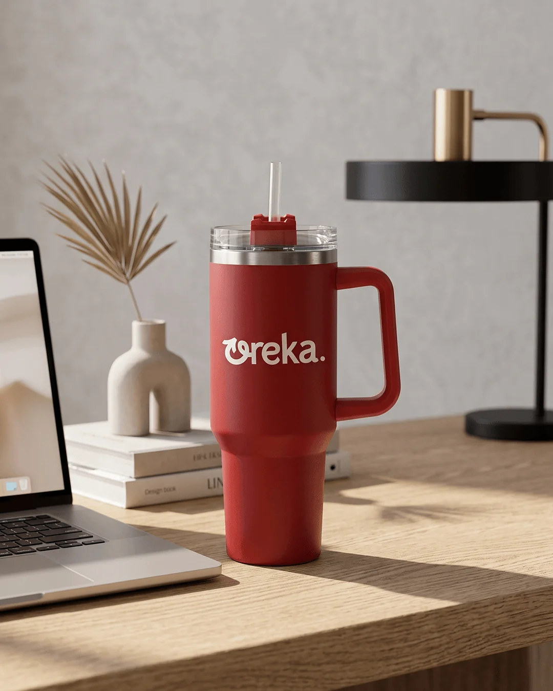 Custom stainless steel travel mugs on an office desk beside a laptop with the logo facing out