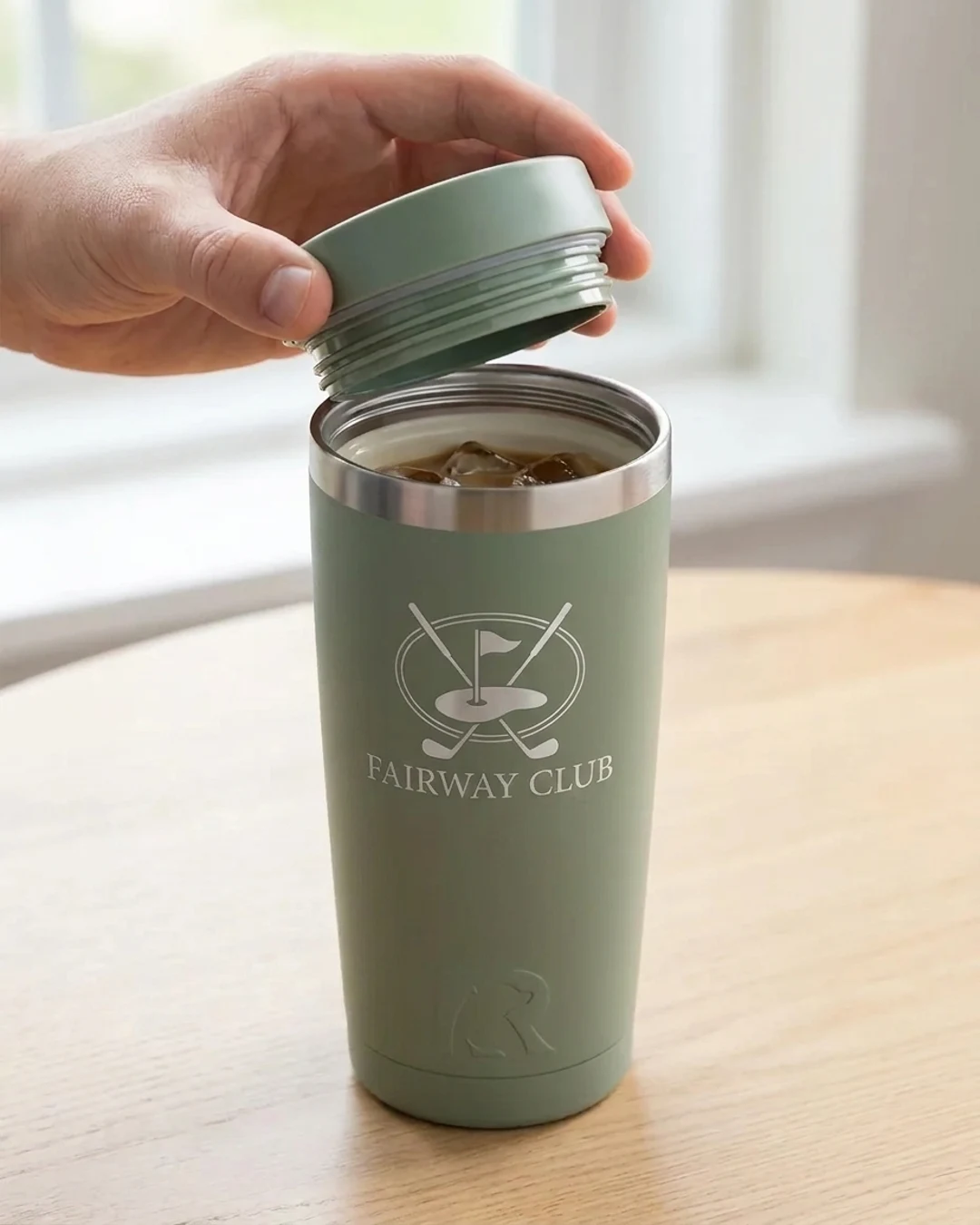Close-up of a custom RTIC tumbler in Sage with the double-threaded lid lifted to show the ceramic lined interior and an engraved golf club logo