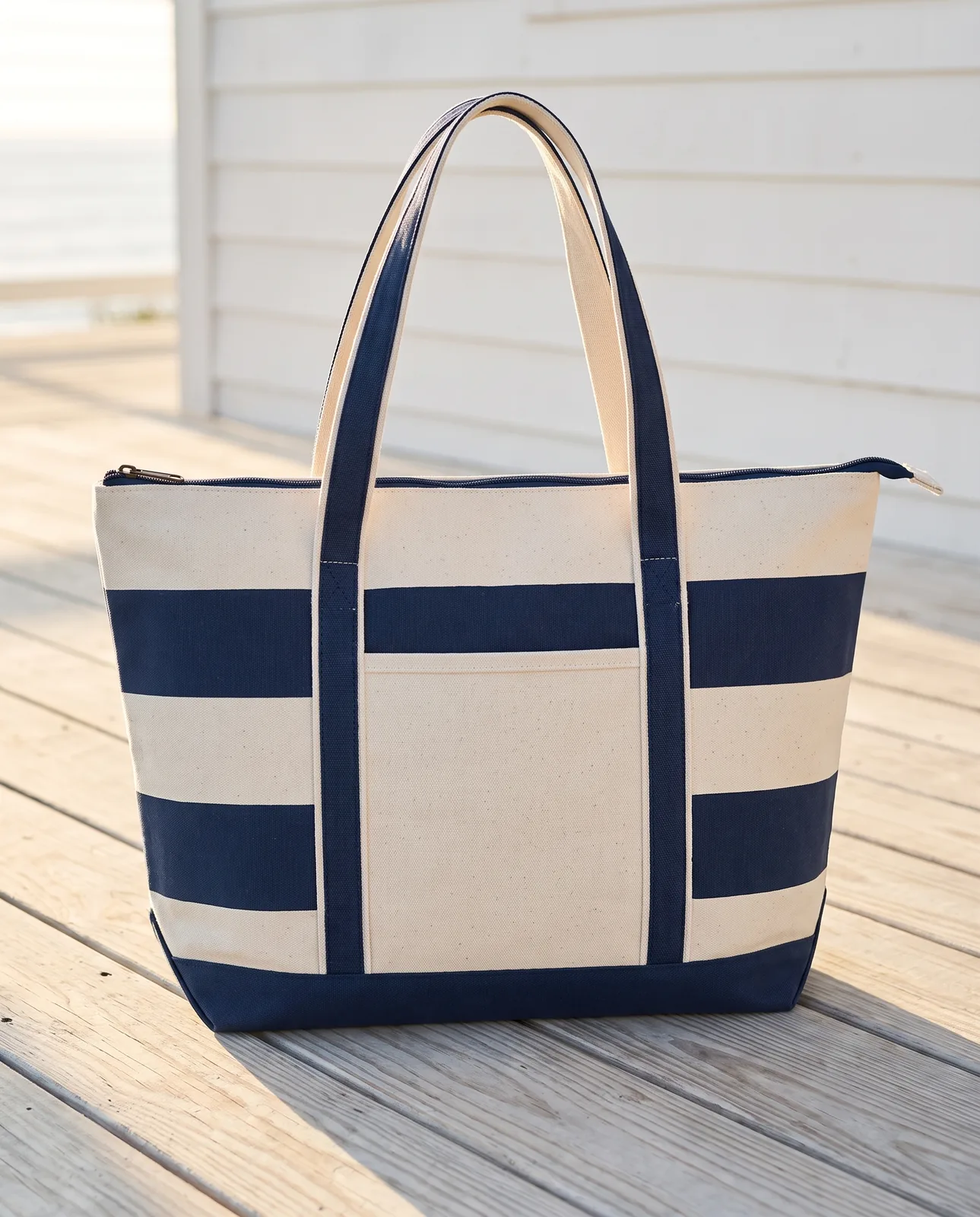 Custom boat totes with zipper in Natural / Navy Blue, 18 oz striped canvas standing on a porch deck