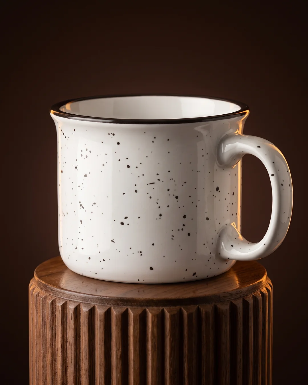 White 7.5 oz campfire mug close up on a walnut plinth, showing the black speckled glaze, flared rim and dark rim line