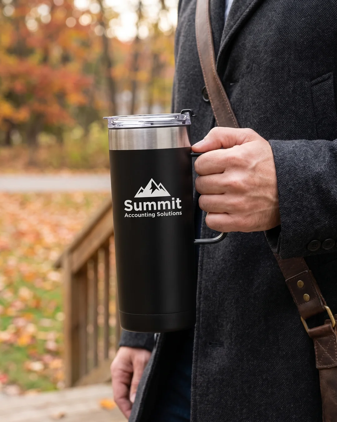 Man in a wool overcoat carrying a black custom coffee tumbler by its handle on an autumn morning