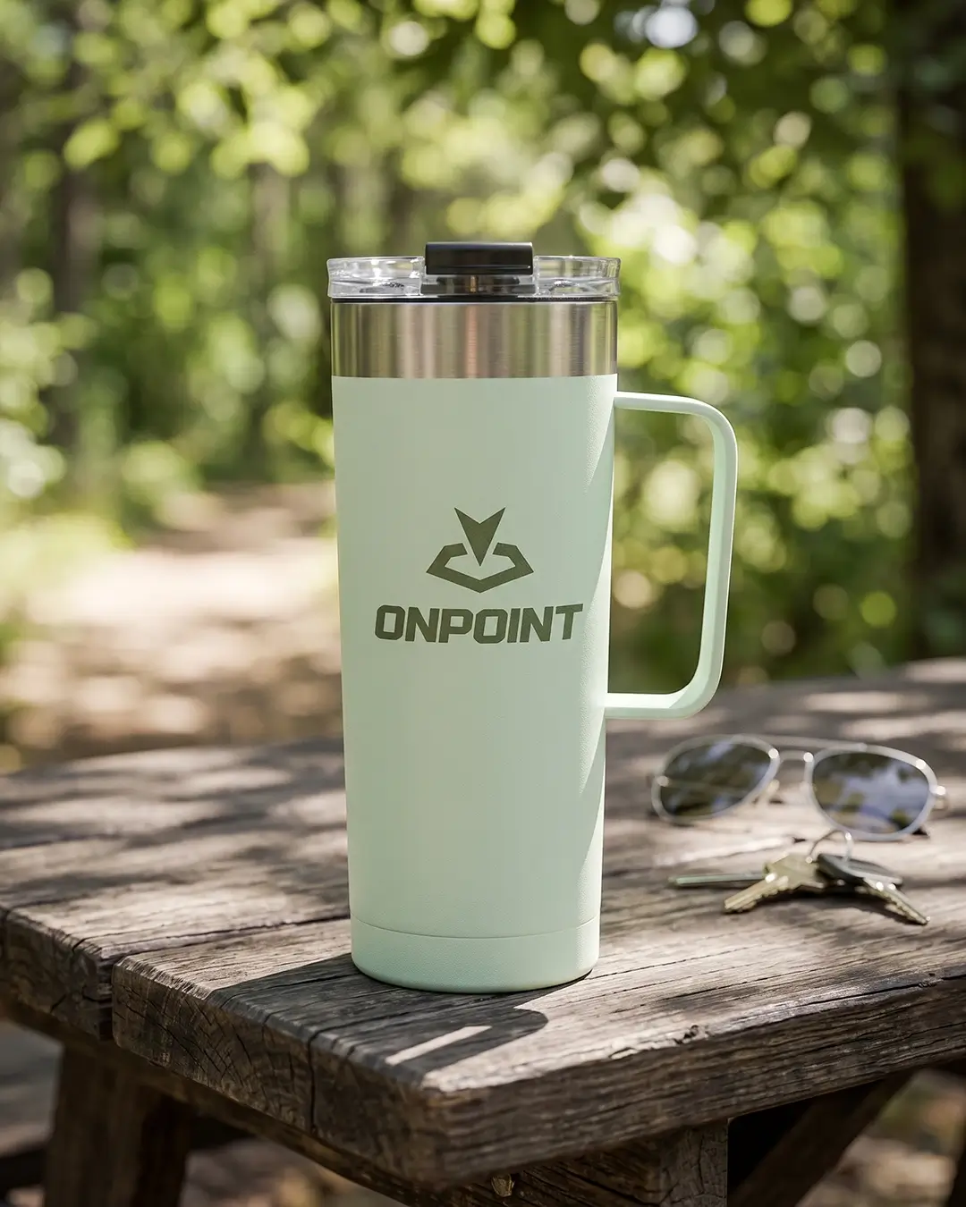 Soft green custom coffee tumbler with a printed logo on a wooden picnic table outdoors