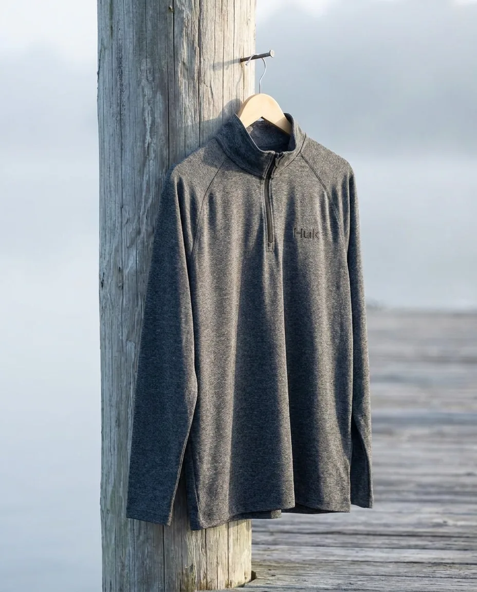 Custom embroidered quarter zips, HUK Airweight heather pullover in charcoal on a hanger at a dock