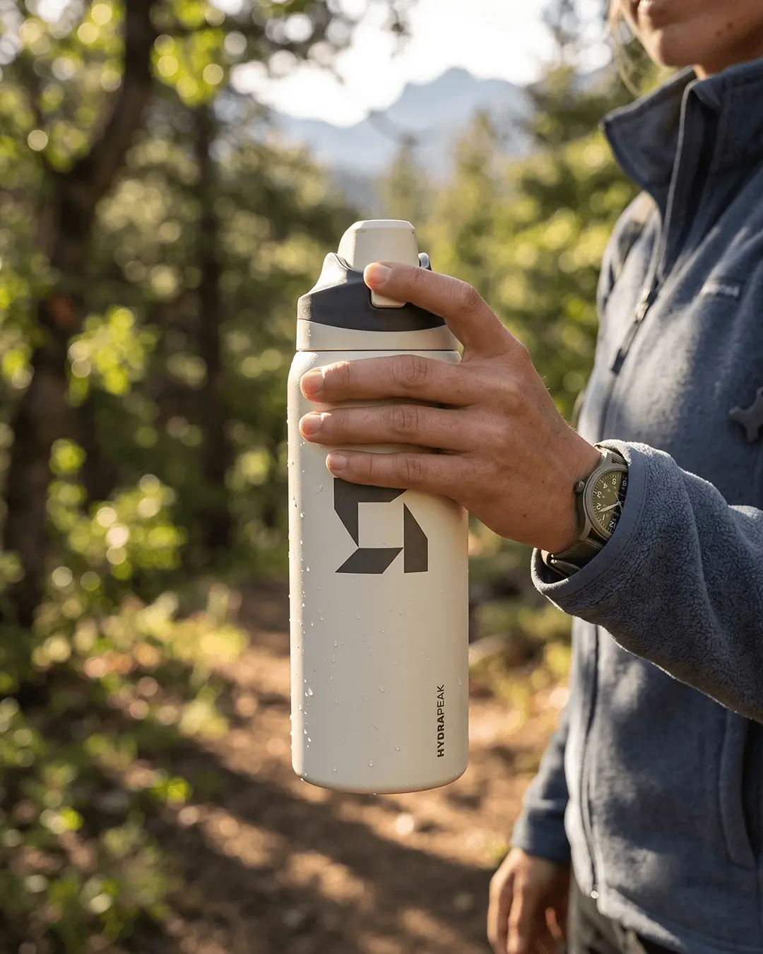 Hiker holding a custom Hydrapeak 32 oz Oasis water bottle with a logo on a forest trail