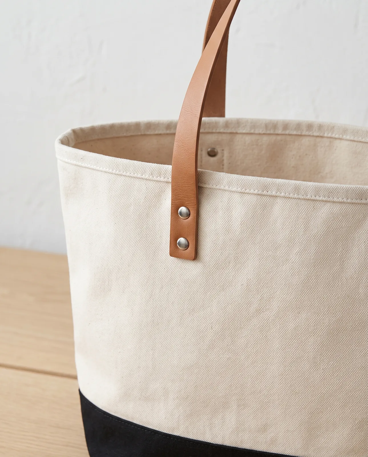 Custom large tote bags with leather handles close-up, tan vegan leather strap riveted to 18 oz natural canvas above a black base