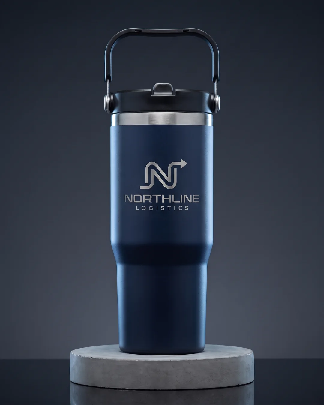 Navy 30 oz custom tumbler with a laser engraved logo in bare steel on a concrete plinth